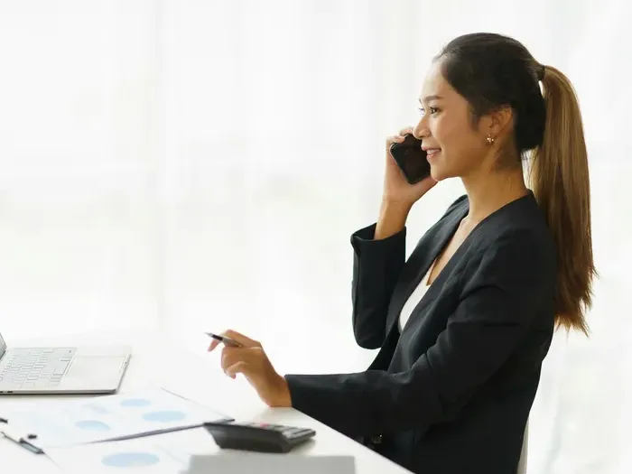 Businesswoman in blazer smiling while on phone at desk, highlighting professional connections with local experts